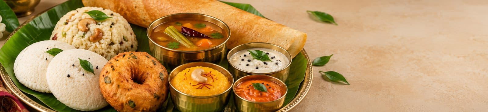 Idli, medu vada, upma and chutneys on a banana leaf